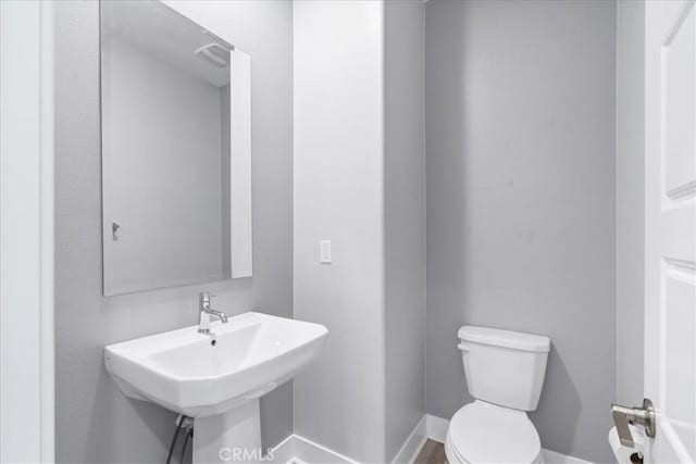 bathroom featuring toilet, baseboards, and a sink