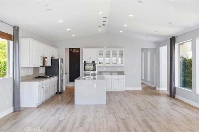 kitchen featuring white cabinets, appliances with stainless steel finishes, a center island with sink, and lofted ceiling