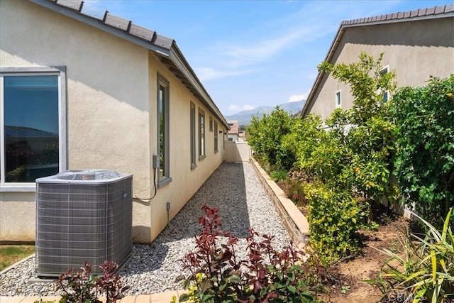 view of home's exterior with central AC, fence, a mountain view, and stucco siding