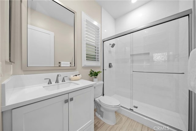 bathroom with toilet, vanity, a stall shower, and wood finished floors
