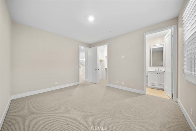 unfurnished bedroom featuring a sink, light colored carpet, baseboards, and ensuite bathroom