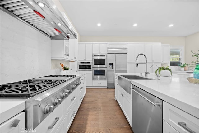 kitchen featuring light countertops, exhaust hood, white cabinets, appliances with stainless steel finishes, and wood finished floors