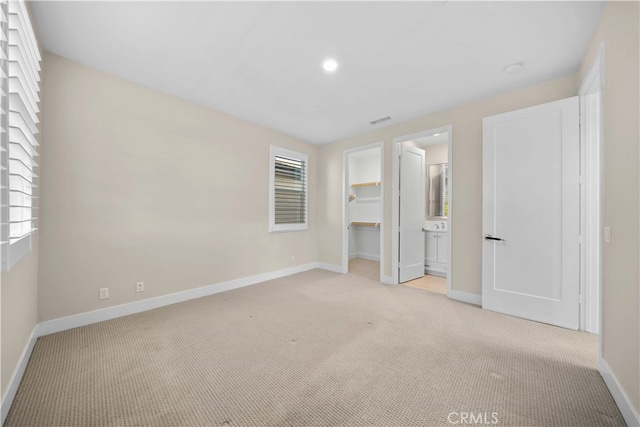 unfurnished bedroom with a spacious closet, visible vents, baseboards, and light colored carpet