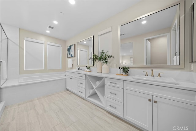 bathroom featuring a shower with door, double vanity, a garden tub, and a sink