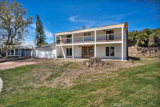 rear view of property with a garage, a balcony, french doors, and stucco siding
