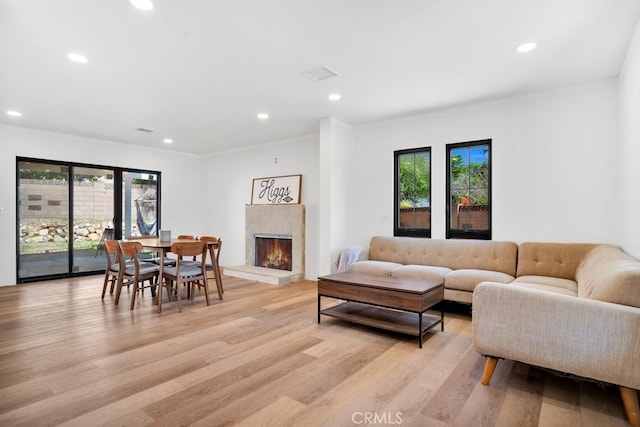 living room with a warm lit fireplace, visible vents, light wood-style flooring, and recessed lighting