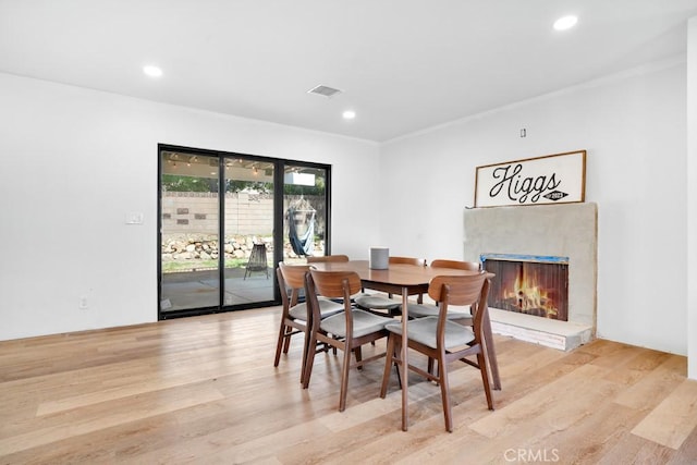 dining area featuring visible vents, light wood-style flooring, recessed lighting, and a premium fireplace