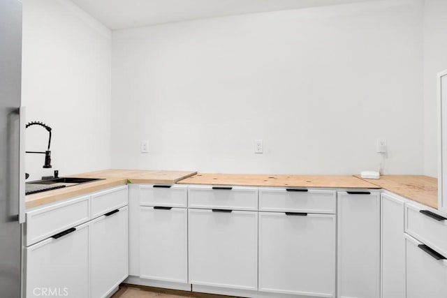 kitchen with butcher block counters, white cabinetry, and a sink