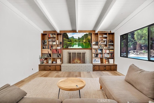 living area with a brick fireplace, beamed ceiling, and wood finished floors