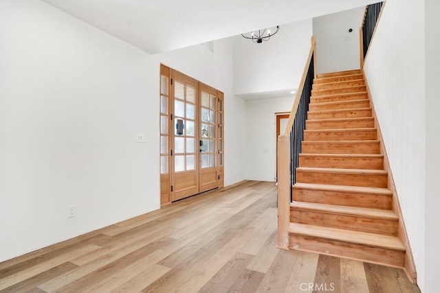 staircase featuring french doors, a towering ceiling, a chandelier, and wood finished floors