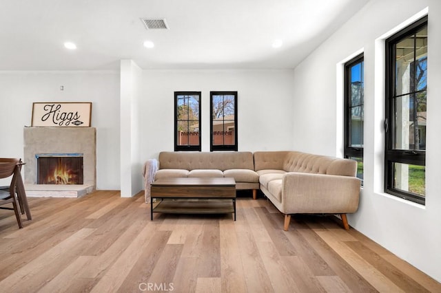 living area with a wealth of natural light, light wood finished floors, visible vents, and a warm lit fireplace