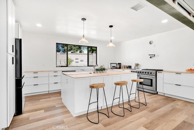kitchen with a breakfast bar, light wood-type flooring, a kitchen island, white cabinets, and high end stove