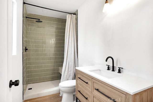 bathroom featuring toilet, tiled shower, vanity, and wood finished floors