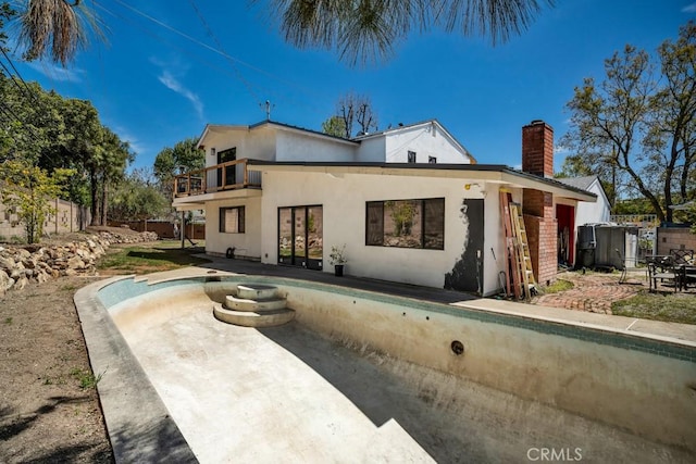 back of house featuring a patio, a balcony, stucco siding, a chimney, and fence