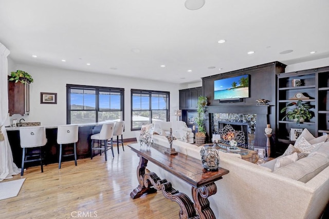 living room with recessed lighting, light wood-style flooring, and a warm lit fireplace