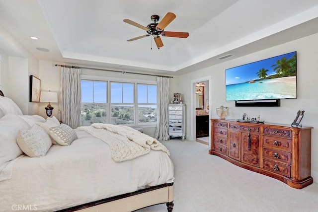 carpeted bedroom with a raised ceiling, ceiling fan, ensuite bath, and visible vents