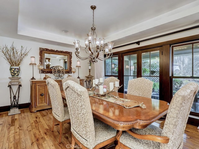 dining space with baseboards, light wood-style flooring, a tray ceiling, and an inviting chandelier
