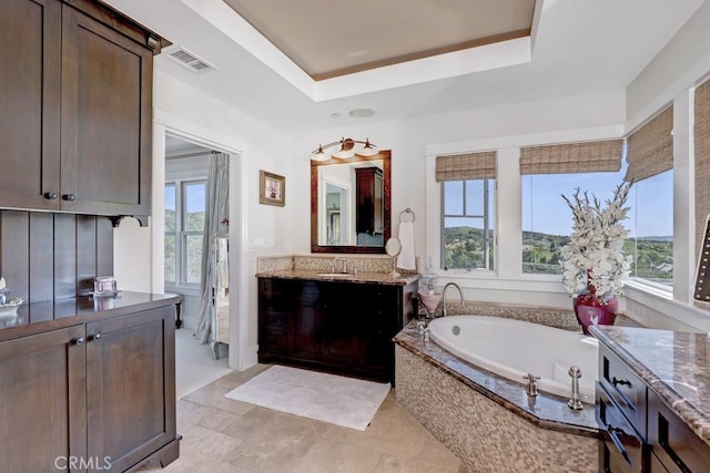 full bath with a raised ceiling, a garden tub, vanity, and visible vents