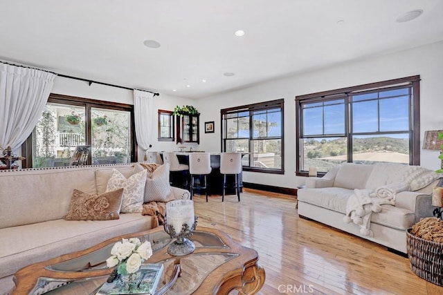 living area featuring baseboards, light wood-type flooring, recessed lighting, and a healthy amount of sunlight