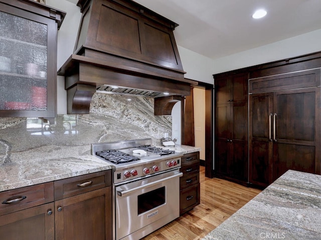 kitchen featuring dark brown cabinets, light wood finished floors, premium stove, light stone countertops, and decorative backsplash