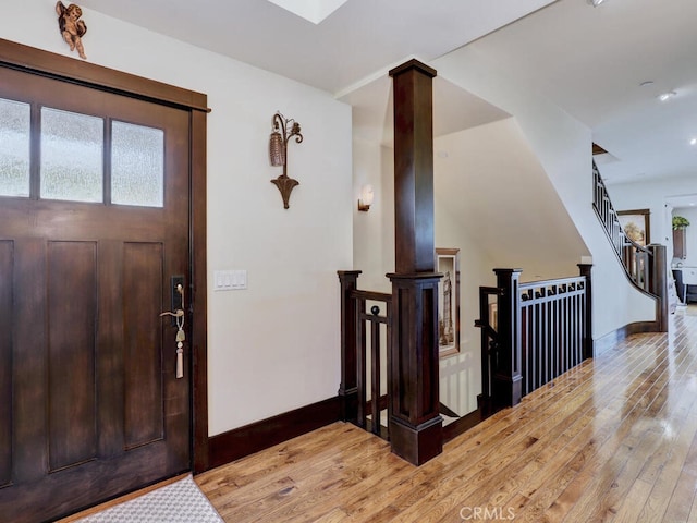 foyer featuring baseboards, light wood finished floors, ornate columns, and stairs