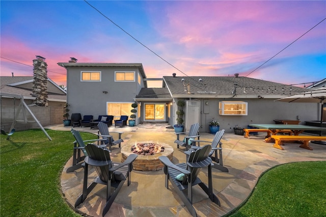 rear view of property with a yard, an outdoor fire pit, fence, and stucco siding