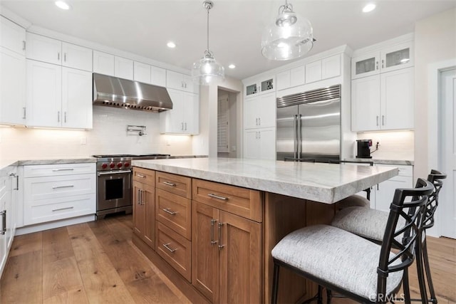 kitchen with high end appliances, glass insert cabinets, extractor fan, and dark wood-type flooring