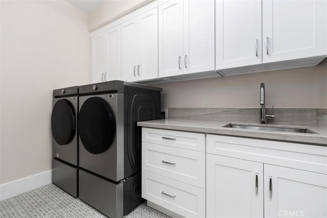 clothes washing area with light floors, independent washer and dryer, cabinet space, a sink, and baseboards