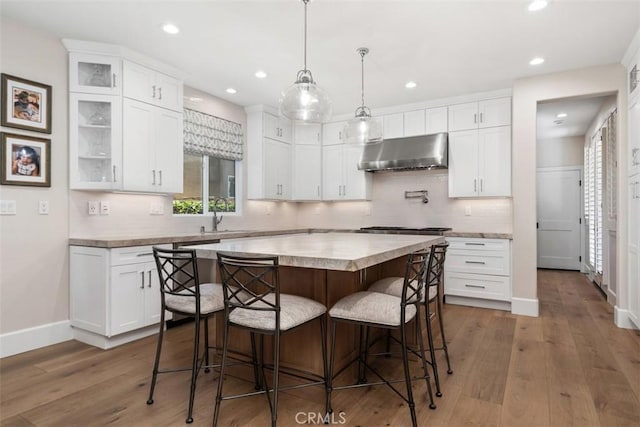 kitchen featuring recessed lighting, under cabinet range hood, a kitchen island, backsplash, and a kitchen breakfast bar