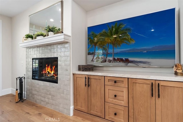 interior space with a glass covered fireplace, light wood-style flooring, and baseboards