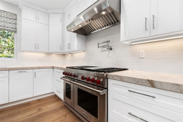 kitchen featuring light wood-style flooring, decorative backsplash, extractor fan, white cabinets, and range with two ovens