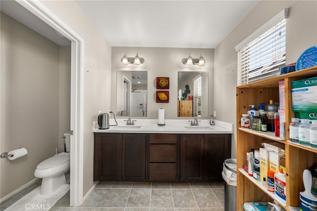 bathroom with toilet, double vanity, a sink, and baseboards