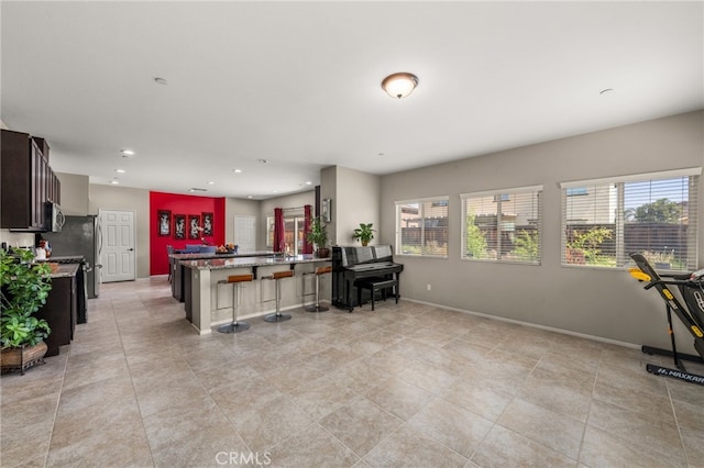 kitchen with a kitchen bar, a peninsula, stone counters, recessed lighting, and baseboards