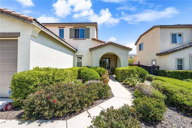 view of front of house with a tiled roof, an attached garage, fence, and stucco siding