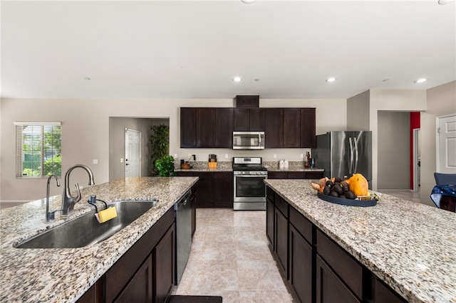 kitchen with dark brown cabinetry, recessed lighting, light stone countertops, appliances with stainless steel finishes, and a sink
