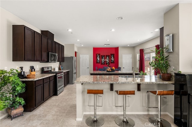 kitchen featuring a sink, appliances with stainless steel finishes, dark brown cabinetry, a peninsula, and a breakfast bar area