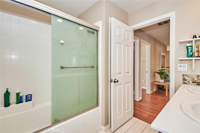 bathroom featuring visible vents, a sink, enclosed tub / shower combo, double vanity, and wood finished floors