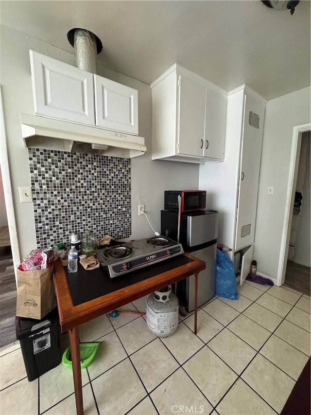 kitchen featuring light tile patterned floors, black microwave, white cabinetry, and decorative backsplash