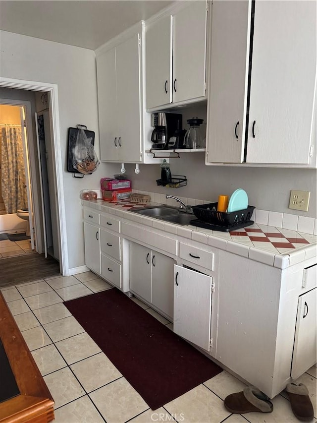 kitchen featuring a sink, tile counters, white cabinetry, and light tile patterned floors