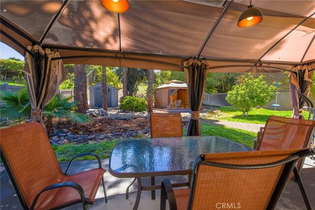 view of patio / terrace featuring a fenced backyard, a shed, a gazebo, an outbuilding, and outdoor dining space
