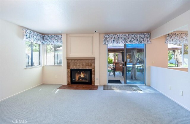 unfurnished living room featuring a tiled fireplace, carpet floors, baseboards, and a healthy amount of sunlight