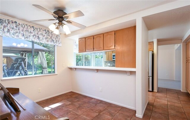 kitchen with freestanding refrigerator, baseboards, ceiling fan, a breakfast bar area, and light countertops