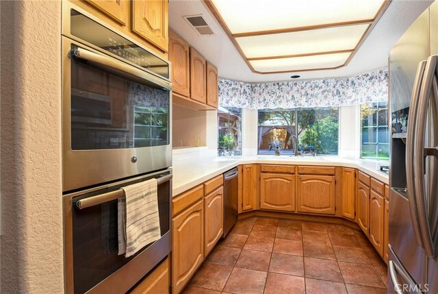 kitchen with appliances with stainless steel finishes, a sink, light countertops, dark tile patterned floors, and visible vents