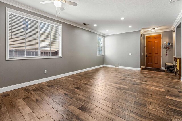 spare room with ceiling fan, ornamental molding, visible vents, baseboards, and dark wood-style floors