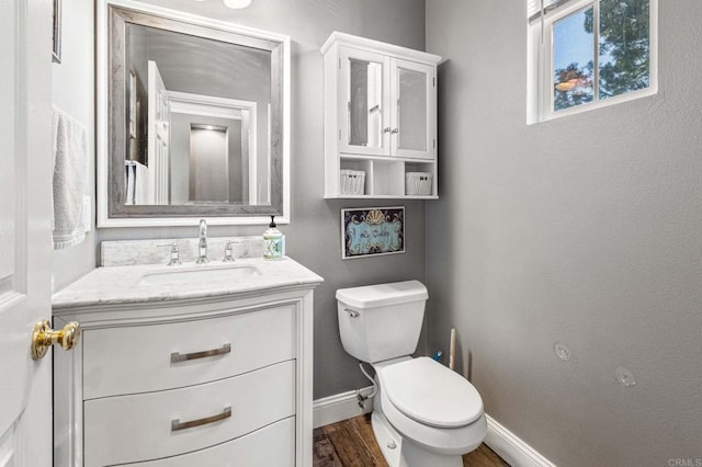 bathroom with toilet, vanity, wood finished floors, and baseboards