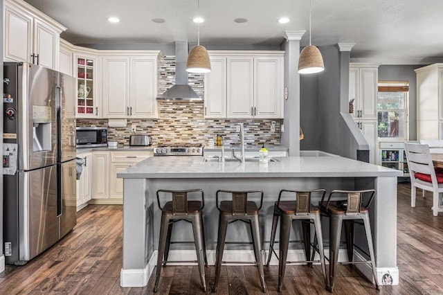 kitchen featuring a sink, wall chimney range hood, dark wood finished floors, stainless steel appliances, and backsplash