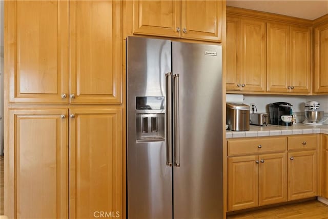 kitchen with light wood-style flooring, high end fridge, and tile counters
