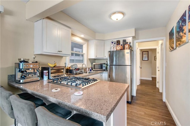 kitchen featuring a sink, light wood-type flooring, stainless steel appliances, white cabinets, and a peninsula