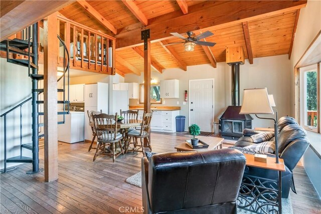 living area with a wood stove, stairs, light wood-style floors, vaulted ceiling with beams, and wood ceiling