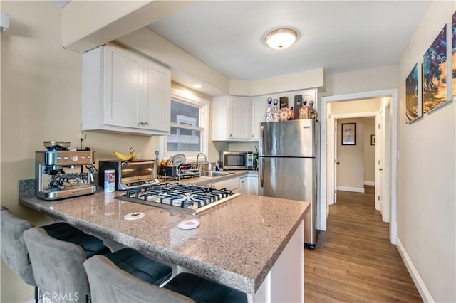 kitchen featuring white cabinets, a peninsula, light wood finished floors, a sink, and appliances with stainless steel finishes